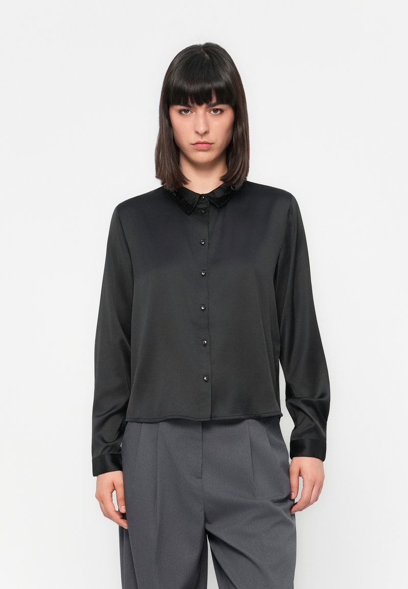 Blusa de satin preta com fecho de botão na frente, colarinho pequeno e mangas longas; textura suave com botões brilhantes e um ajuste confortável.