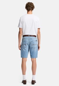 Jasnoniebieskie szorty dżinsowe o luźnym kroju, z dwiema tylnymi kieszeniami i brązowymi detalami szycia, zestawione z gładką białą koszulką.