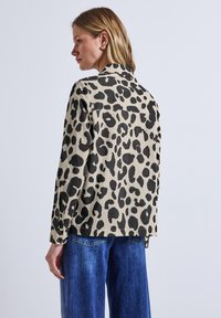 Leopardenmusterhemd in Beige und Schwarz, mit langen Ärmeln, Knopfmanschetten und Rückenpasse, kombiniert mit lockeren blauen Denim-Jeans.