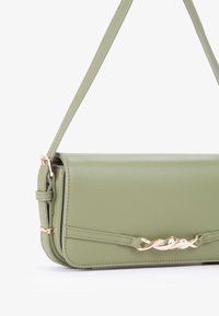 Borsa a mano verde in ecopelle con una texture liscia, forma rettangolare e un accento in catena dorata sul fronte, dotata di una sottile tracolla regolabile.