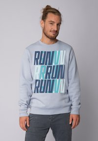 Hellblaues Sweatshirt mit einem auffälligen, geschichteten "RUN"-Grafikdesign in verschiedenen Blautönen. Es hat lange Ärmel und gerippte Bündchen.