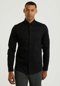 Camisa negra de manga larga con cuello, cierre de botones en el frente y detalles en los hombros. Textura suave con un sutil logo en el pecho.