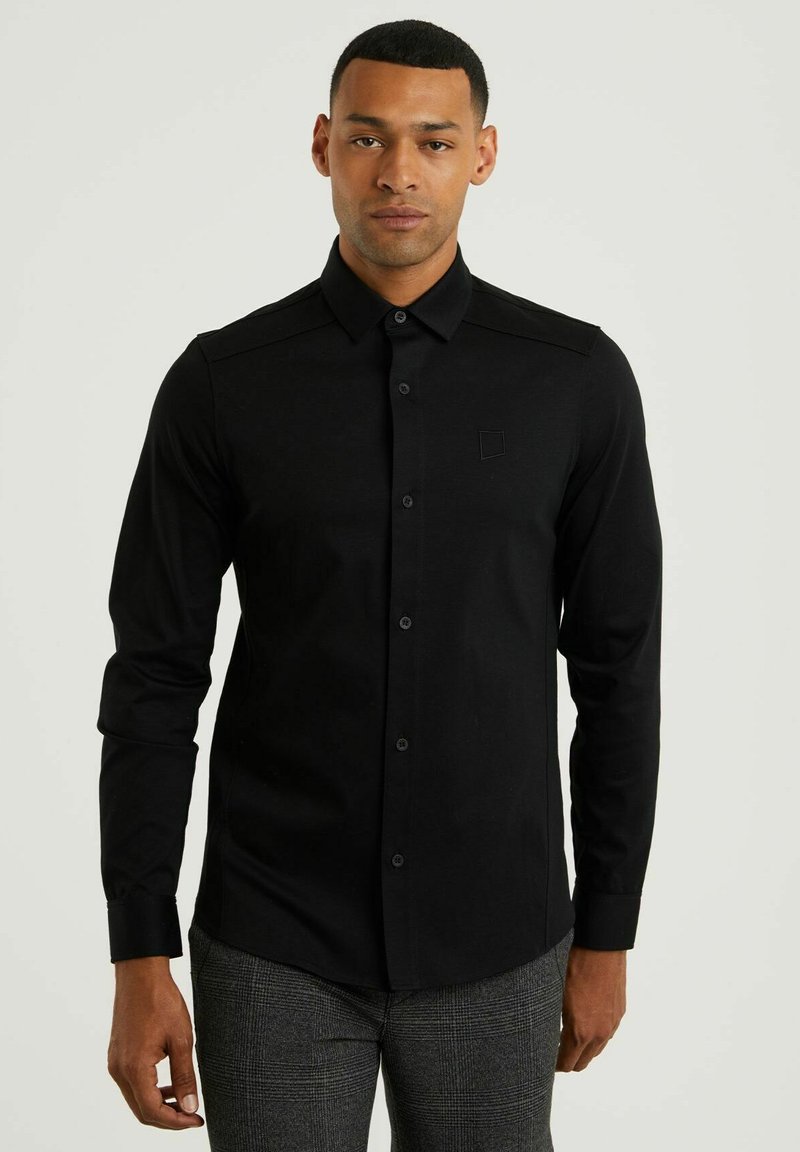 Camisa negra de manga larga con cuello, cierre de botones en el frente y detalles en los hombros. Textura suave con un sutil logo en el pecho.