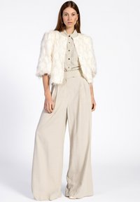 Witte textuur cropped jas met korte mouwen, gecombineerd met een lichtgrijs overhemd met knopen en brede broeken.