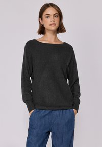 Pullover grigio scuro, morbido e leggermente svasato, con scollatura ampia a barca e maniche lunghe, realizzato in tessuto morbido e texturizzato. Indossato con pantaloni blu.