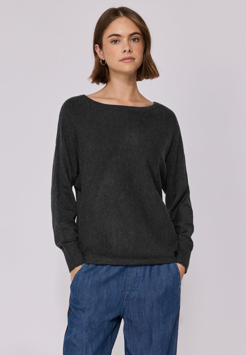 Pullover grigio scuro, morbido e leggermente svasato, con scollatura ampia a barca e maniche lunghe, realizzato in tessuto morbido e texturizzato. Indossato con pantaloni blu.