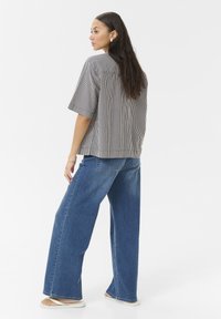 Haut à manches courtes rayé noir et blanc, associé à un jean large bleu clair, présenté de dos avec une coupe décontractée.
