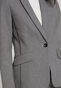 Grijs-zwart geruit colbert met een ingesneden revers, enkele knoopsluiting, twee steekzakken aan de voorkant en een textuurrijke stofafwerking.