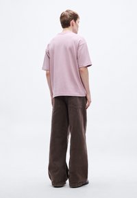 Fialkové bavlnené tričko s krátkymi rukávmi, kombinované s voľne strihanými hnedými kordurovými nohavicami s vreckami na zadnej strane, pohľad zozadu.
