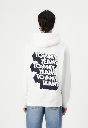 Hvit hettegenser med stor, tydelig "TOMMY JEANS" tekst i svart på baksiden, med vanlig passform og kengurulomme foran.