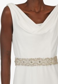 Weißes Kleid mit drapiertem Cowl-Ausschnitt, tailliert mit einem gold- und silberfarbenen, mit Juwelen bestickten Gürtel. Glatte, weiche Stofftextur.