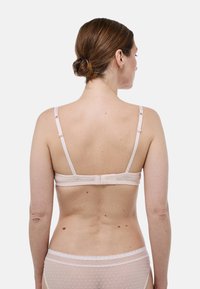 Soutien-gorge rose clair avec des bretelles ajustables doubles, texture à pois et un système de fermeture à crochets à l'arrière. Une douce bordure en dentelle souligne la bande.