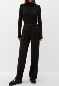 Black long-sleeve turtleneck top in a textured fabric, paired with high-waisted, wide-leg black trousers and chunky black shoes with metal accents.
