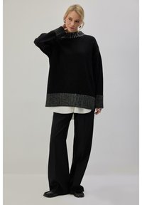 Pull noir surdimensionné avec un col et des poignets à rayures métalliques texturées, associé à un pantalon noir à jambes larges. Fini en tissu lisse.