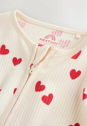 Kremowy, prążkowany kombinezon dla niemowląt z czerwonymi wzorami serc, z przednim zamkiem błyskawicznym i miękkim dekoltem. Metka z napisem „NEXTbaby” i tęczowym logo.