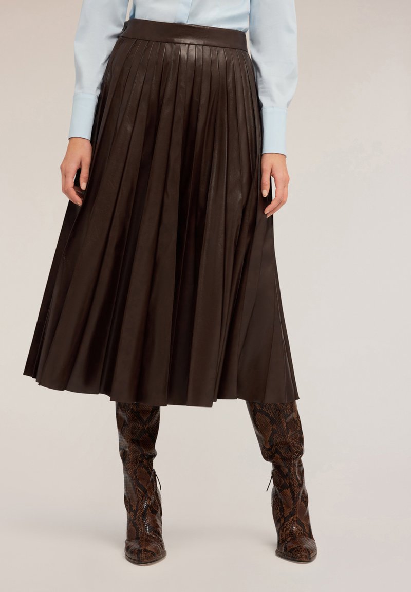 Falda plisada de cuero marrón con una cinturilla alta, combinada con botas hasta la rodilla de estampado de serpiente. Textura suave y diseño fluido.