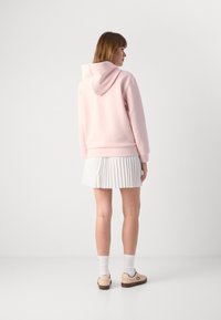 Hanorac roz cu glugă, asociat cu o fustă plisată albă. Pantofi bej și șosete albe compun ținuta. Design minimal și textură moale.