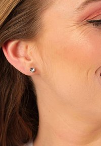 Boucles d'oreilles claires en forme de gemme ronde, montées en métal argenté, présentées en gros plan sur une oreille. Présentent une surface scintillante et un design simple.