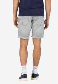 Man standing facing away wearing light gray rolled-up shorts, navy blue shirt, white socks with gray stripes, and black sneakers.