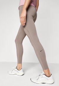 Lyse brune leggings med høy midje, med konturerte sømmer og en liten svart logo. Kombinert med hvite treningssko.