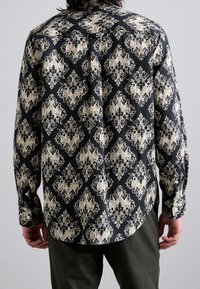 Camicia a maniche lunghe in tessuto nero con motivo damascato crema. Il design include motivi floreali e vorticosi intricati.