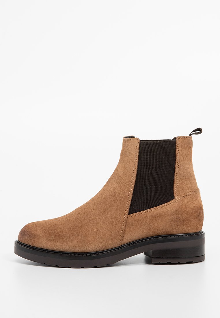 Bota de ante marrón hasta el tobillo con paneles laterales elásticos, punta redonda y tacón bajo en bloque. Textura suave con acentos oscuros contrastantes.
