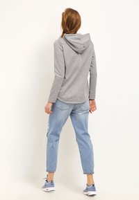Sweat-shirt à capuche gris avec une coupe décontractée, des manches longues et un ourlet arrondi. Porté avec un jean déchiré léger bleu clair taille haute.