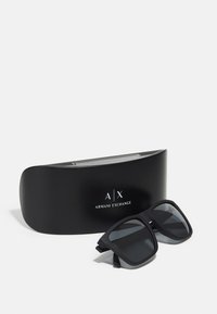 Ochelari de soare patrati negri cu lentile întunecate și finisaj mat, poziționați lângă un toc elegant negru cu logo-ul Armani Exchange.