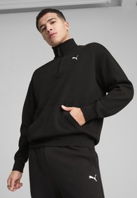 Sort, langærmet zip-up pullover lavet af et glat stof med en kængurulomme og et lille hvidt logo på brystet.