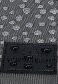 Vízálló, szürke szövet, kiemelkedő átlátszó cseppekkel, fekete címkével, amelyen „JOHNNY URBAN” felirat van belepréselve, valamint további vízcseppek a címkén.