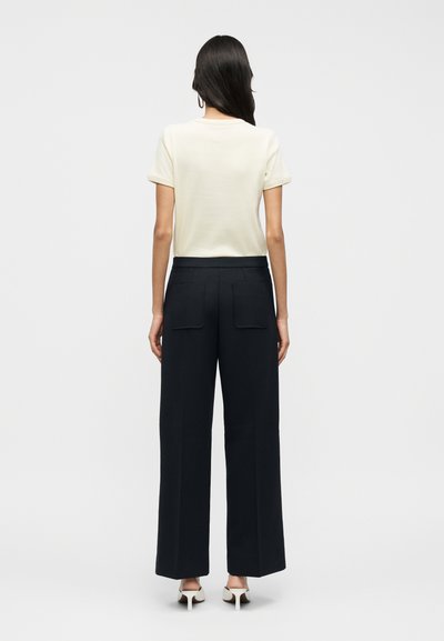 Ανοιχτό μπεζ μπλουζάκι με ριγμένα μανίκια, συνδυασμένο με σκούρο παντελόνι φαρδύ στα πόδια με δύο πίσω τσέπες. Καθαρός, μίνιμαλ σχεδιασμός.