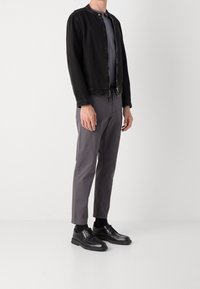 Svart jeansjacka med rund hals och dragkedja, kombinerad med grå chinos och svarta snörskor. Minimalistisk design, skräddarsydd passform.