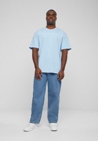 T-shirt en coton bleu clair à manches courtes et coupe décontractée, avec un design de texte en cursive blanche à l'avant. Assorti à un jean bleu ample.