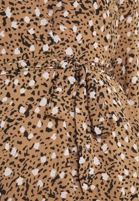 Tejido marrón con manchas abstractas en blanco y negro, atado en un lazo bien hecho a la cintura de una prenda.