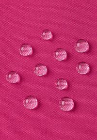 Przezroczyste krople wody na fakturowanej różowej powierzchni tkaniny, ukazujące gładki, okrągły kształt i wyraźne krawędzie.