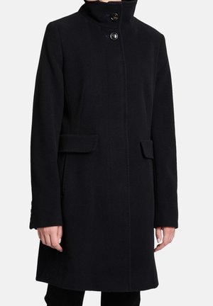 Schwarzer knielanger Mantel mit hohem Kragen, zwei vorderen Pattentaschen und Knopfverschluss, getragen von einer Person mit entspannt an den Seiten hängenden Händen.