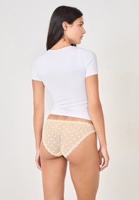 Slip beige a pois con bordino in pizzo, con un accento a fiocco, abbinato a una maglietta bianca aderente a maniche corte. Vista posteriore dell'outfit.