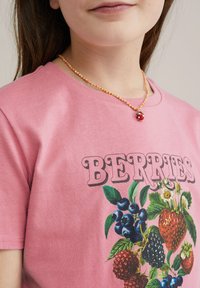 Rožinė medvilninė marškinė su spalvinga uogų grafika ir žodžiu "UOGOS" ryškiu, retro šriftu. Paprasta karoliukų grandinėlė su raudonu pakabuku.