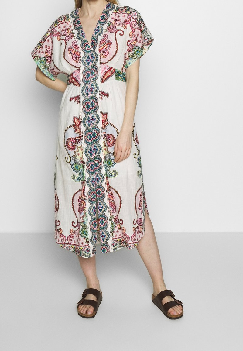 Biała lniana sukienka z kolorowym haftem paisley i kwiatowym, z dekoltem w kształcie litery V i krótkimi rękawami, sięgająca do połowy łydki.