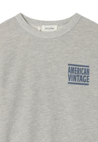 Sweat-shirt gris à col rond avec "AMERICAN VINTAGE" imprimé en bleu sur le côté gauche de la poitrine et une étiquette de marque blanche à l'intérieur du col.