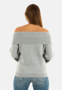 Maglione grigio a spalle scoperte con scollatura a costine, decorato con dettagli glitterati. Tessuto morbido con maniche lunghe e rilassate e un taglio ampio.