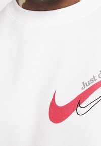 Sudadera blanca con un gran logo de Nike en rojo, un logo más pequeño en negro y el texto "Just Do It" en gris sobre el gráfico.