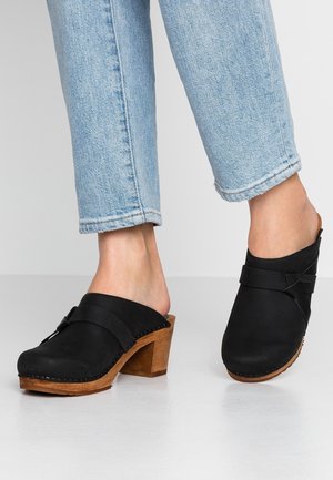 Zwarte suède klompen met een houten hak, voorzien van een decoratieve band en stiksel langs de zool. Gemaakt in combinatie met lichtblauwe denim.