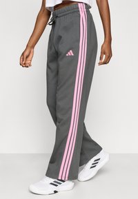 Szare spodnie dresowe z różowymi paskami po bokach i logo Adidas na lewym kieszonce. Posiadają elastyczny pas i luźny krój.