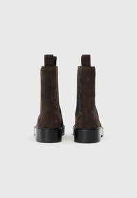 Bottines en daim marron avec des panneaux latéraux élastiques et un talon épais noir. Le design présente une silhouette élégante et une texture lisse.