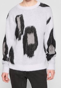 Weißer gestrickter Pullover mit schwarzen und grauen abstrakten Mustern, rundem Halsausschnitt sowie gerippten Bündchen und Saum; weicher, strukturierter Stoff.