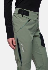 Lichtgroene soft-shell broek met ritszakken, zwarte accenten en logo. Beschikt over een hoge tailleband met knopen en een comfortabele pasvorm.