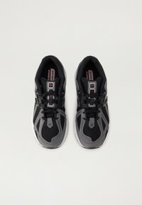 Baskets de sport noires et grises avec tissu en maille, bout arrondi, semelles rembourrées et fermeture à lacets. Présente un logo "NB" sur le côté.