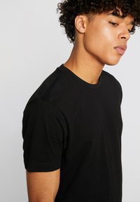 Zwarte katoen t-shirt, ronde hals, korte mouwen, aansluitend ontwerp, zachte textuur, geen zichtbare patronen of accenten. Zijkant gezien met model.