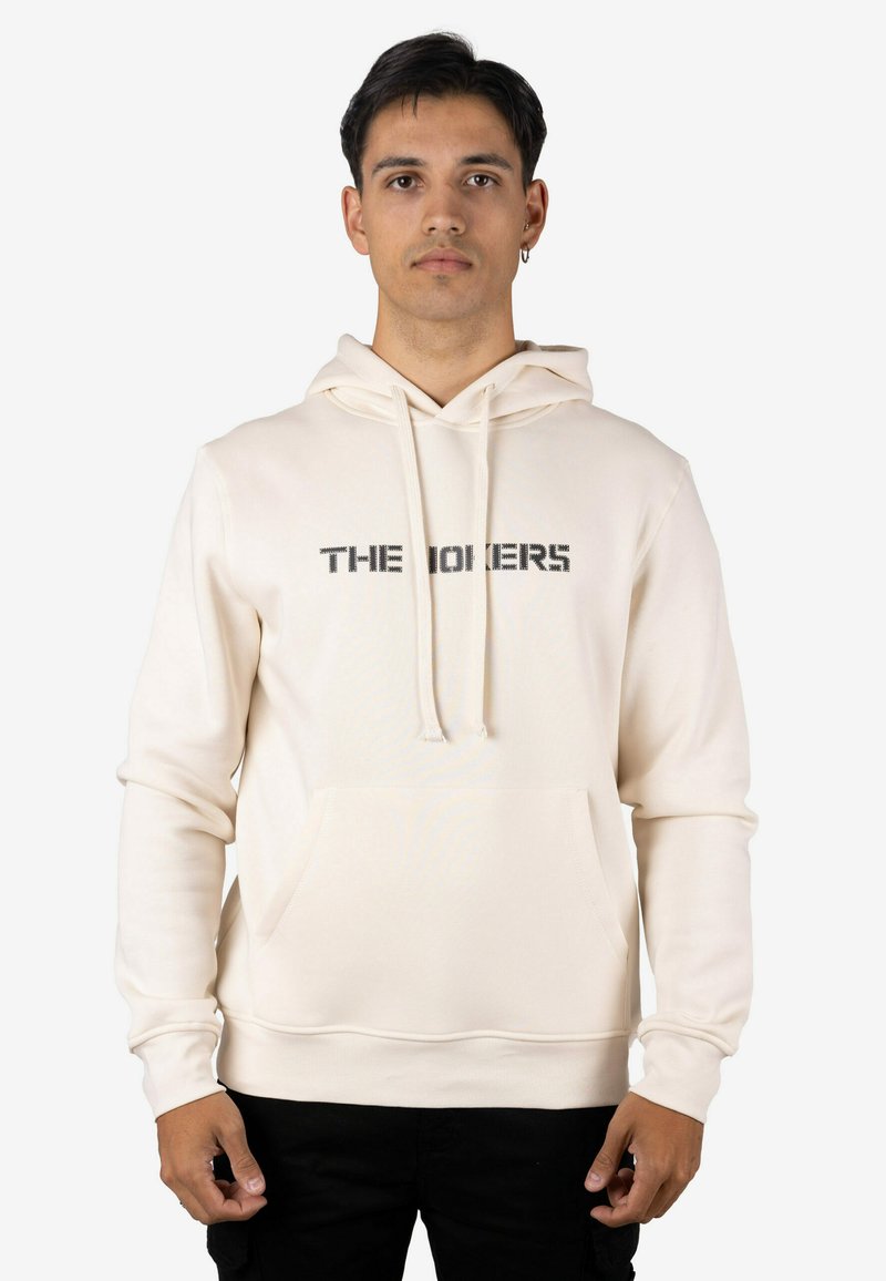 Sudadera con capucha color crema con un bolsillo frontal y un gráfico de texto impreso en negro. Confeccionada con tela suave, de ajuste holgado y capucha ajustable.